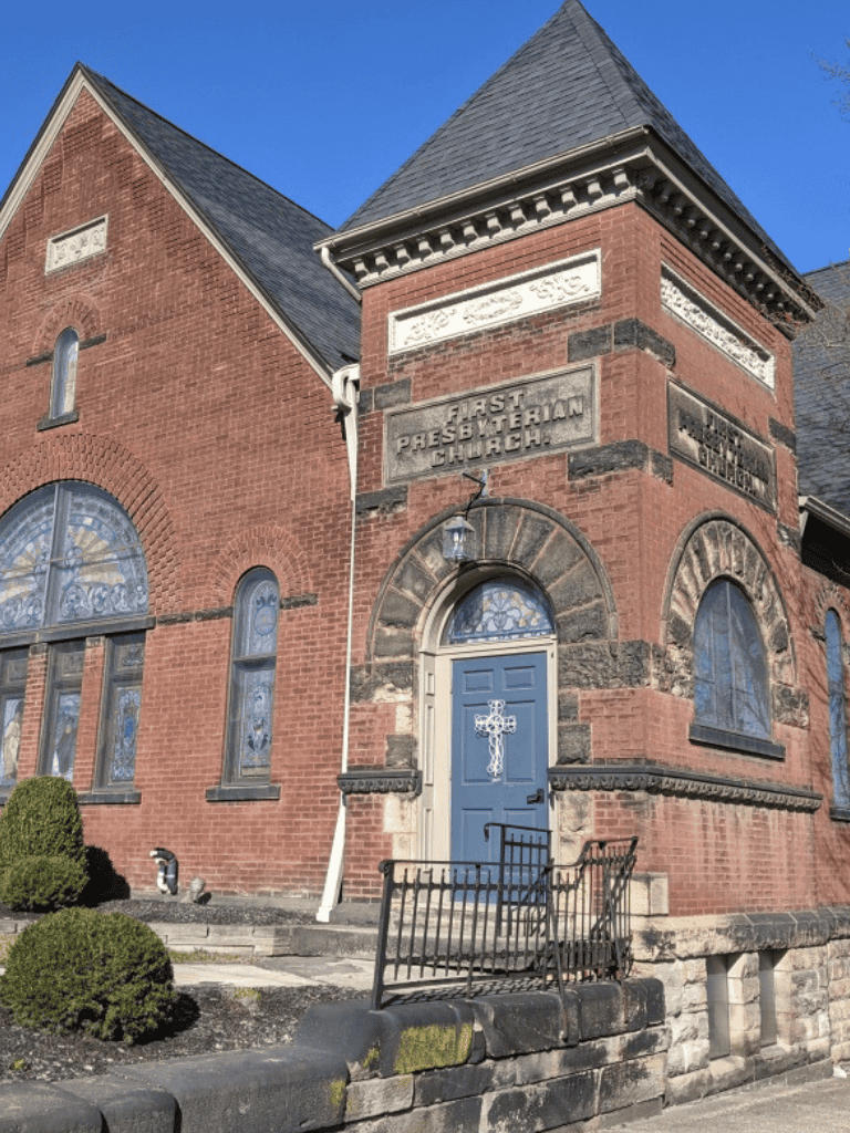 Small church with brick exterior and stained glass windows, labeled First Presbyterian Church, historic architecture, sunny day.