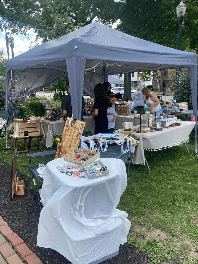 Colorful outdoor craft market booth with handmade jewelry and accessories on display.