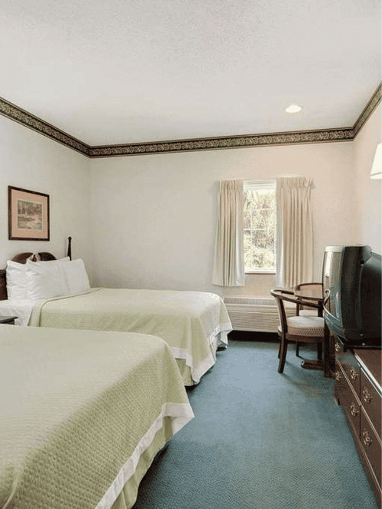 Cozy hotel room with two queen beds, vintage TV, and window with natural light.