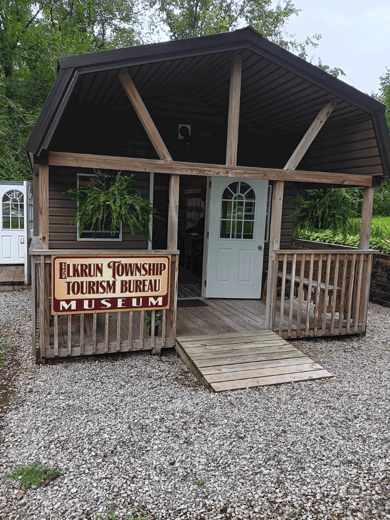 Rustic Elkrun Township Tourism Bureau Museum with porch and greenery.