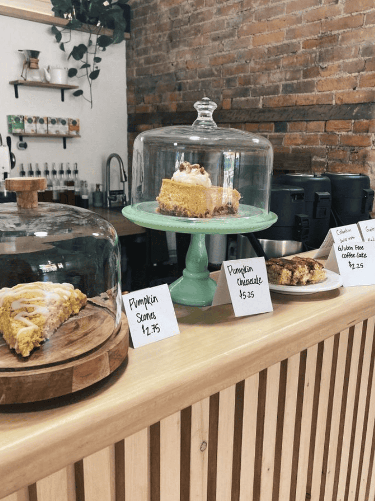 Creamy pumpkin pie slice under glass dome at cozy bakery, perfect for fall dessert lovers.