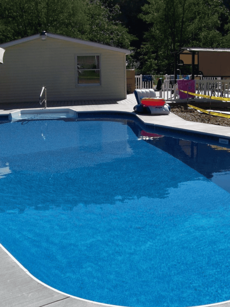 Bright backyard swimming pool with pool accessories and lush green trees in the background.