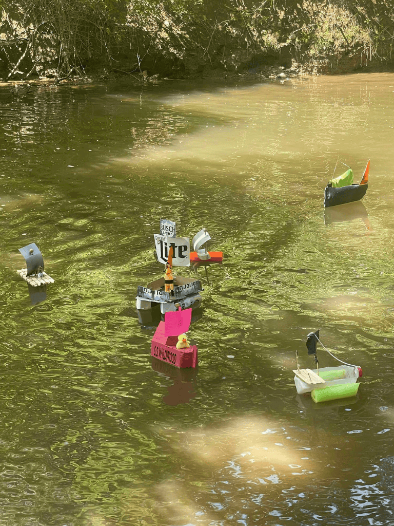 Colorful miniature boats floating on a river, decorated with beer logos and fun accessories.
