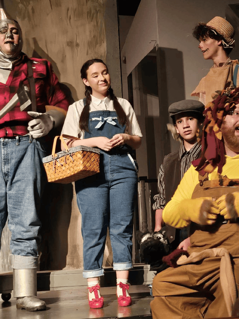 Mysterious theatrical scene with actors in costumes, young girl with braids, and expressive performers, setting a captivating story.