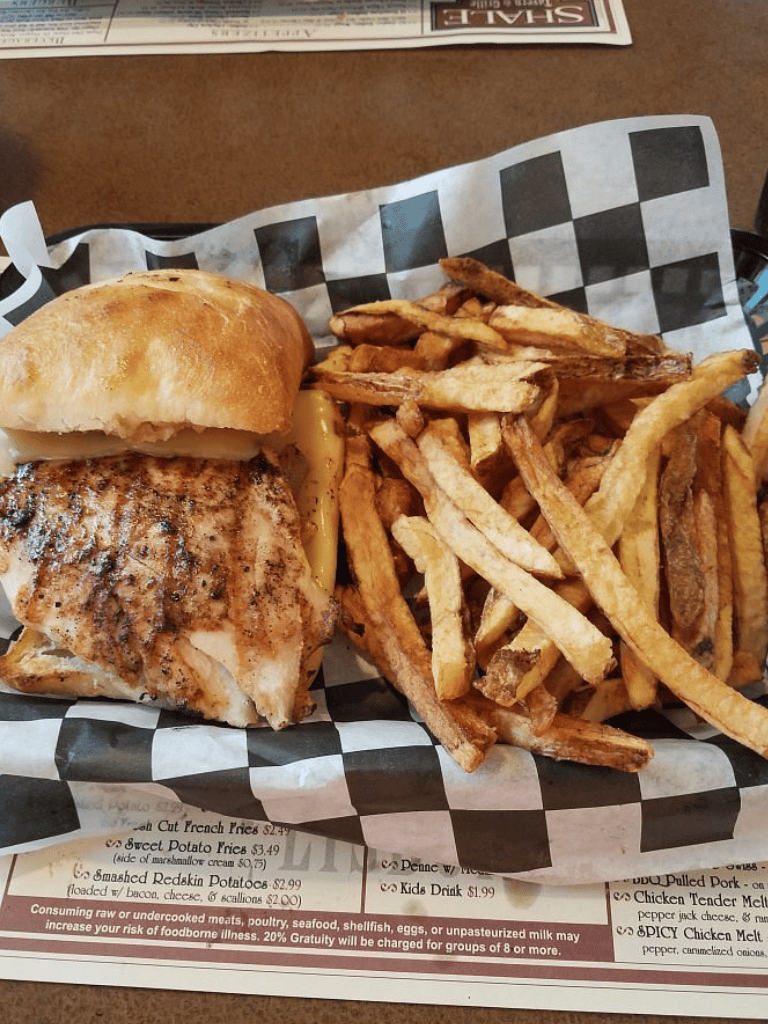 Grilled fish sandwich with crispy fries on checkered paper, served at a casual eatery.