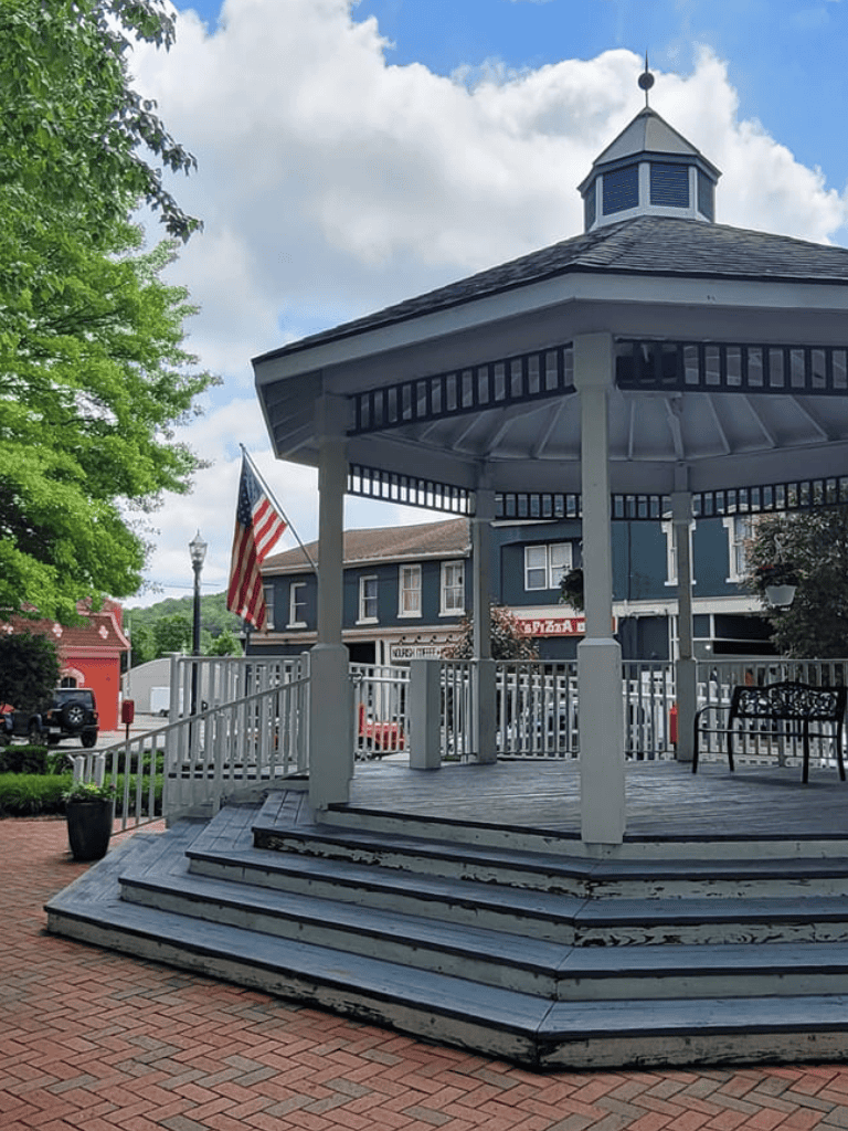 Charming park gazebo with American flag in small-town plaza, perfect for events and gatherings.