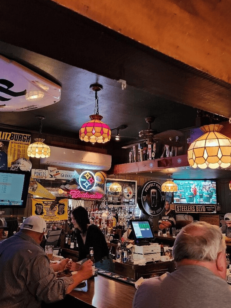 Cozy bar interior with warm lighting, patrons enjoying drinks, and sports on TV screens, perfect for good times and socializing.