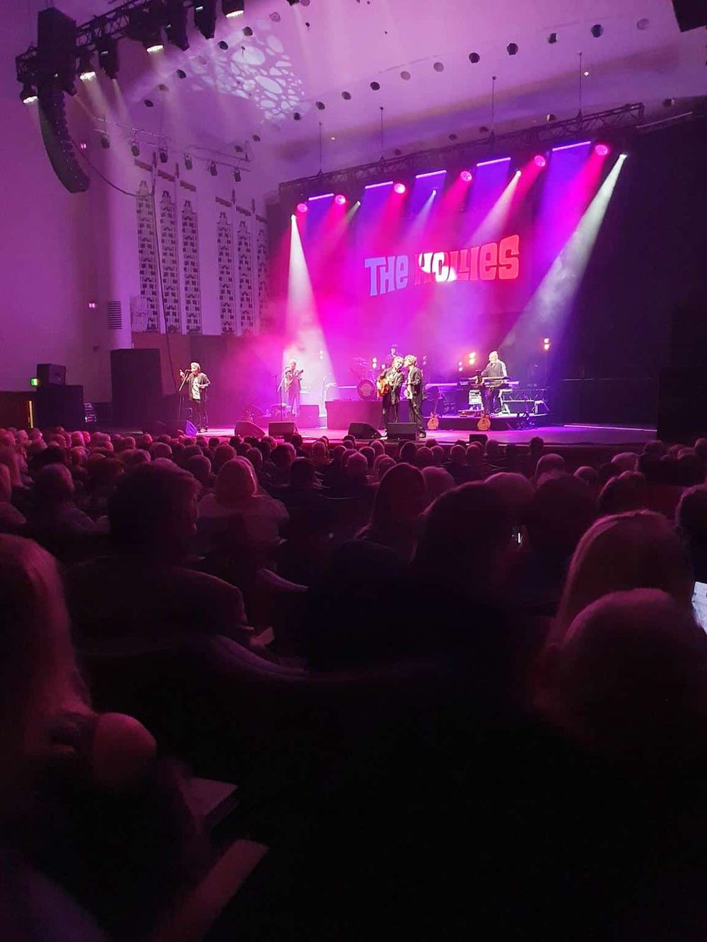 Live concert performance at QuestForDirections, vibrant stage lights, singing band, and crowded audience.