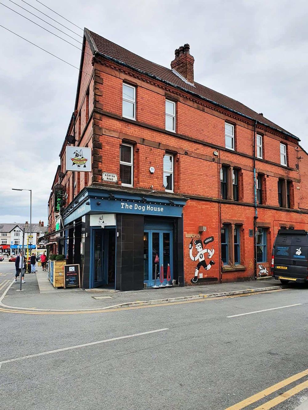 Cozy pub on a street corner in a red brick building, featuring the name "The Dog House" and outdoor seating.