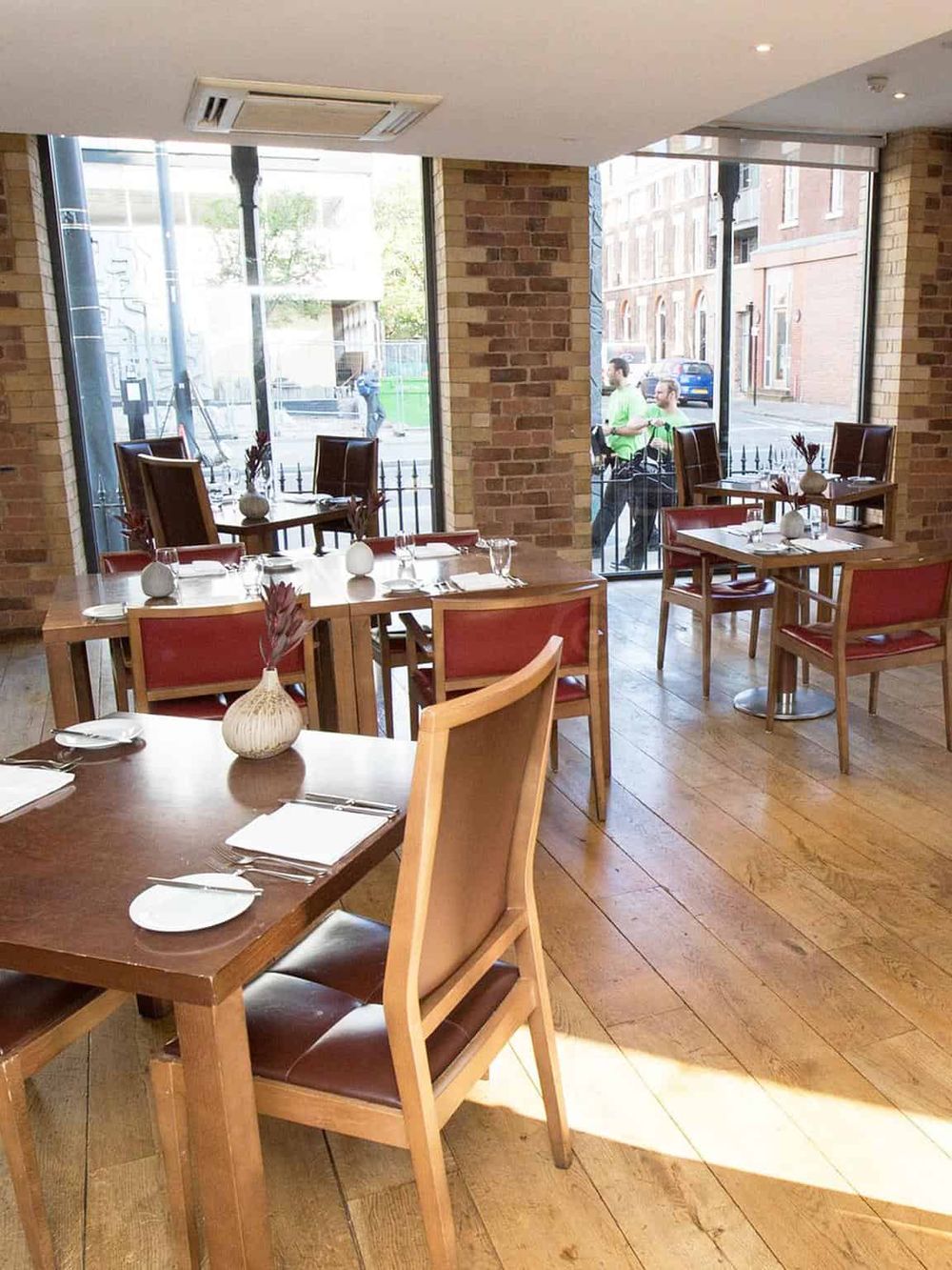 Cozy modern restaurant interior with large windows, wooden tables, and red chairs for a comfortable dining experience.