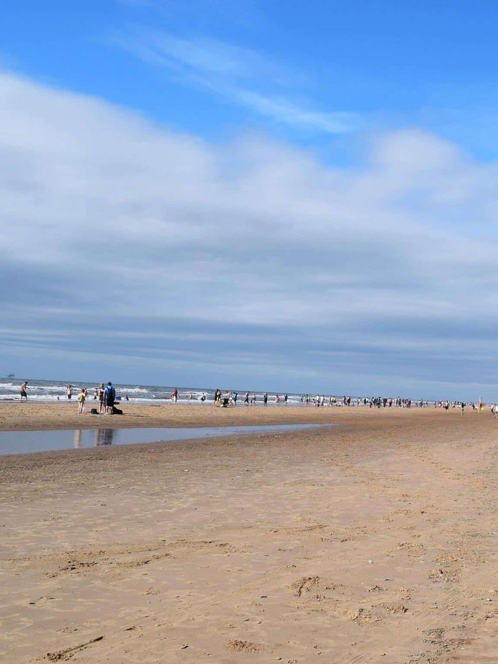 Beach scene with people enjoying sunny day, seaside activities, and ocean views.