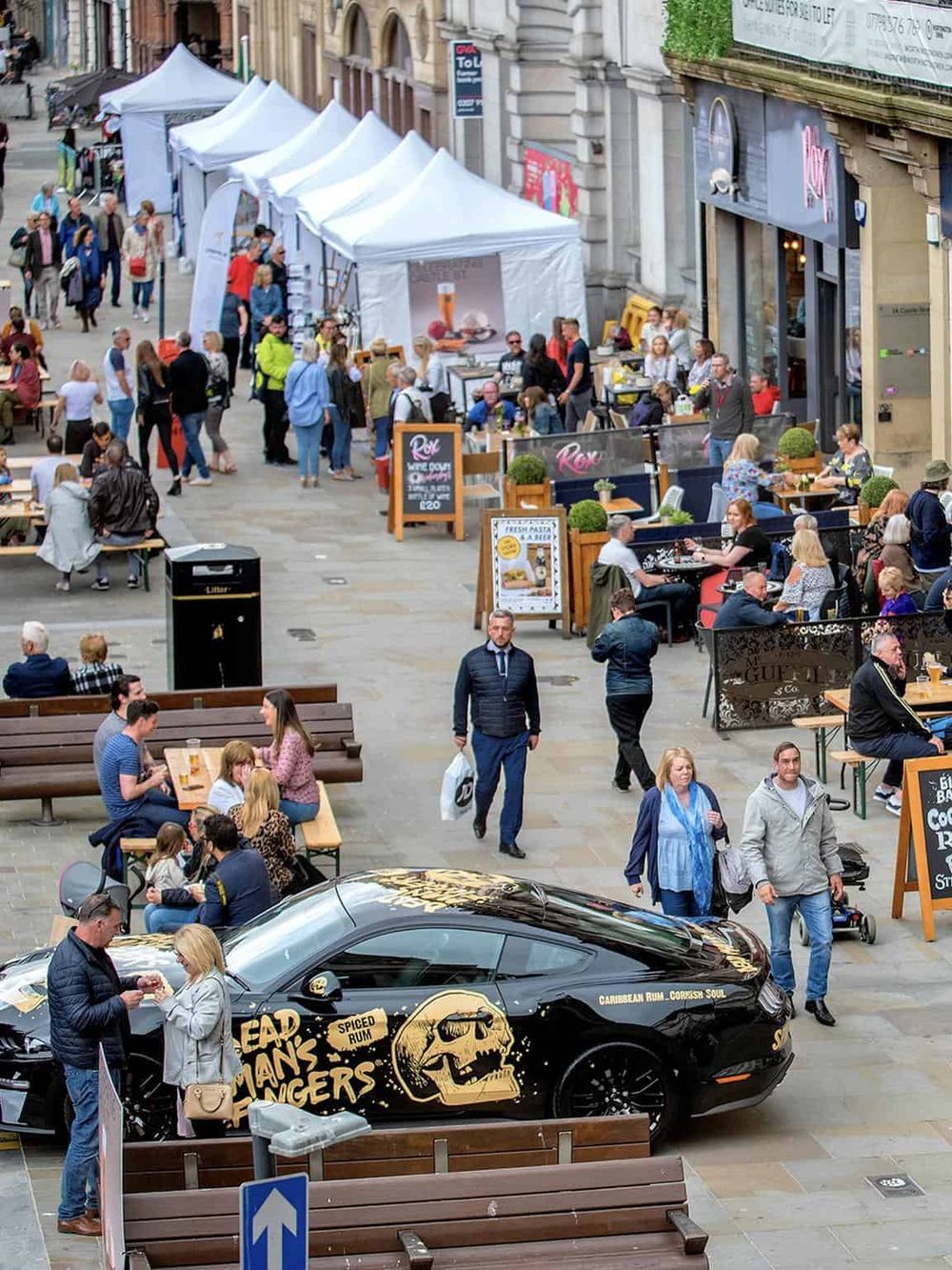 Busy street market with food stalls, outdoor dining, and pedestrians, perfect for exploring local city life and attractions.