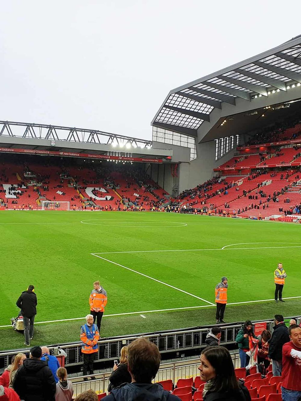 Bright Liverpool football stadium during match day with security staff and cheering fans.