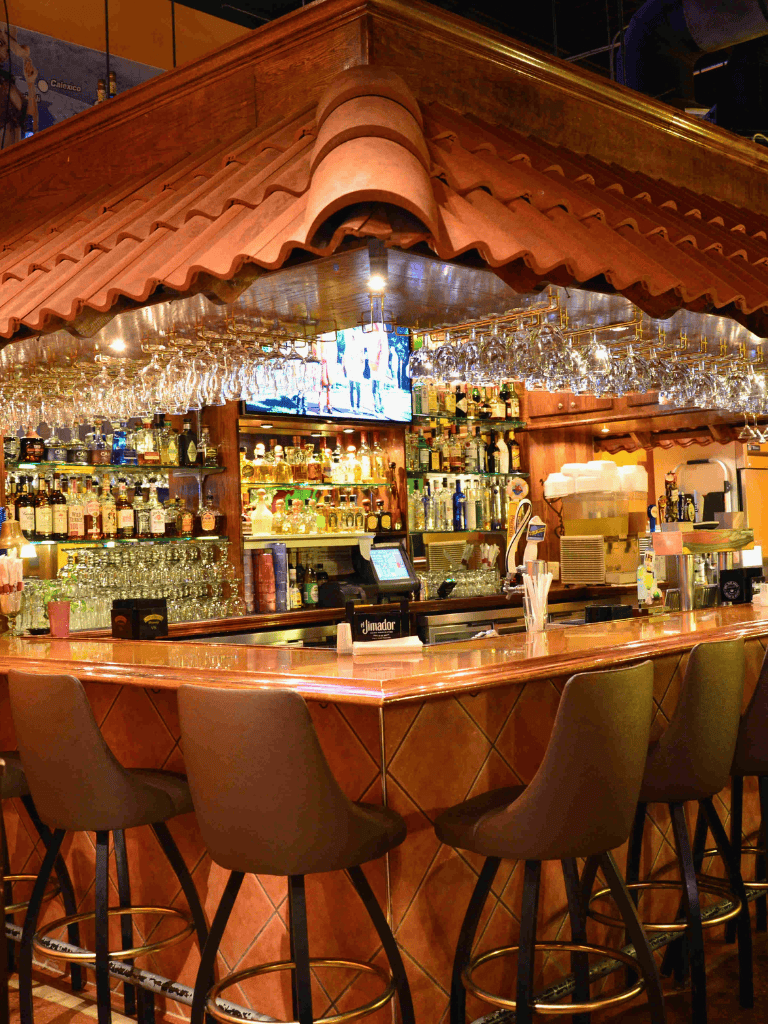 Well-stocked bar with liquor bottles and glassware at a Mexican-themed restaurant.