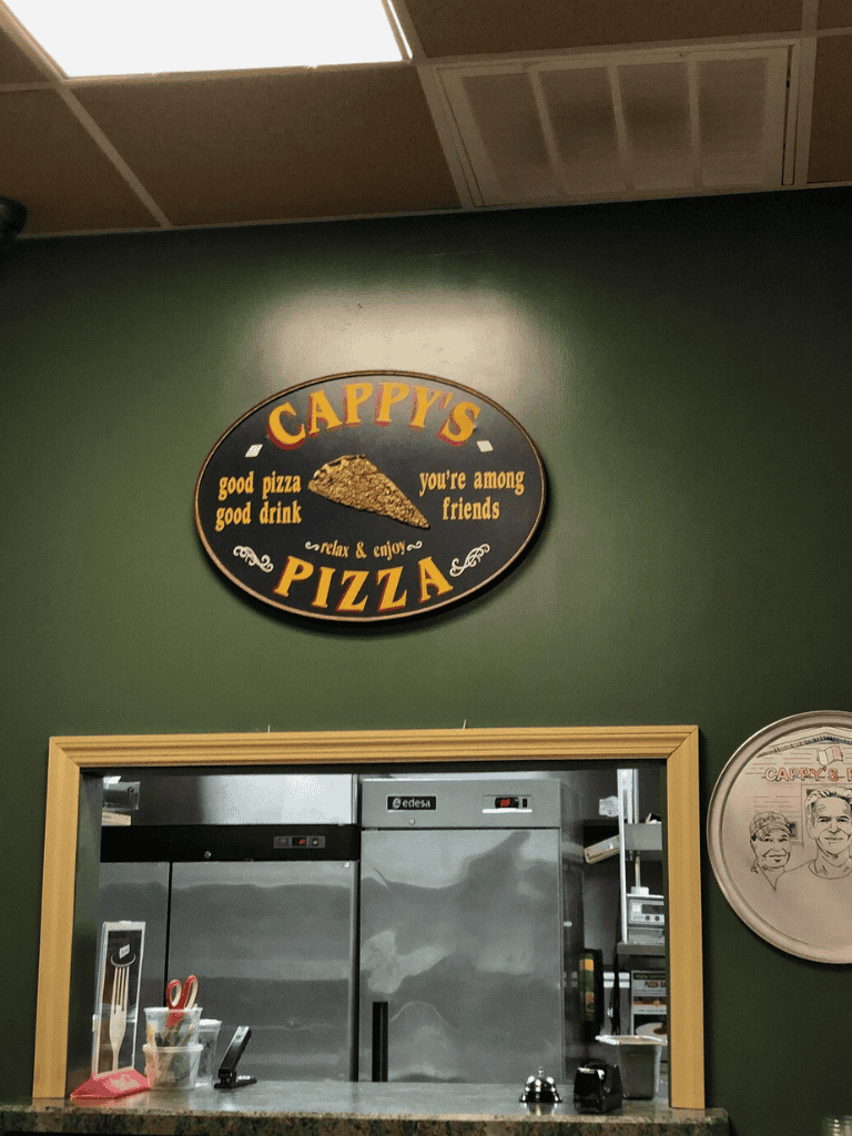 Pizza restaurant interior with a green wall, pizza sign, and equipment for food service.