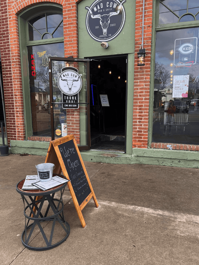 Cozy restaurant entrance with chalkboard sign and outdoor table, serving delicious food in a vibrant town setting.