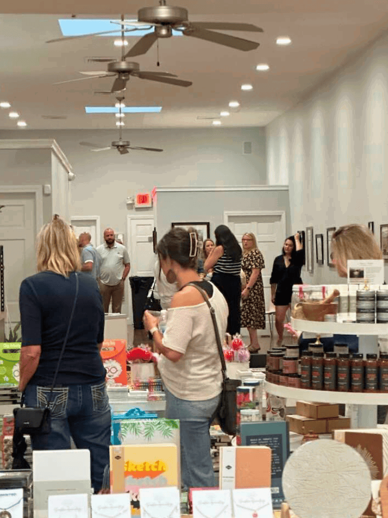 Bright art gallery interior with visitors browsing artwork and products, ideal for exploring local art scenes and purchasing unique gifts.