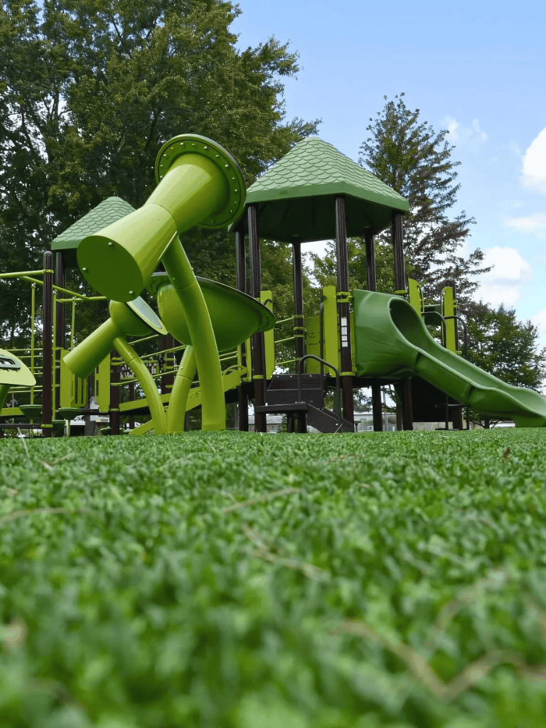 Colorful playground equipment with slides and tunnels in a park setting, surrounded by trees and a bright blue sky.