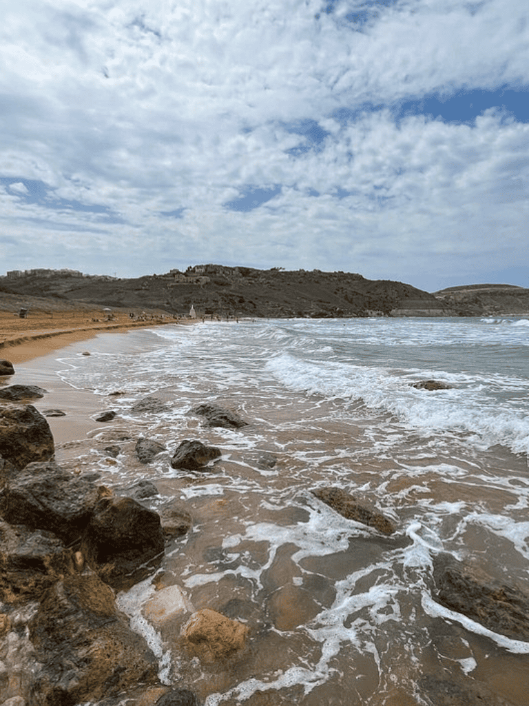 Relaxing beach with rocks, shoreline, and ocean waves under partly cloudy sky — perfect coastal destination.