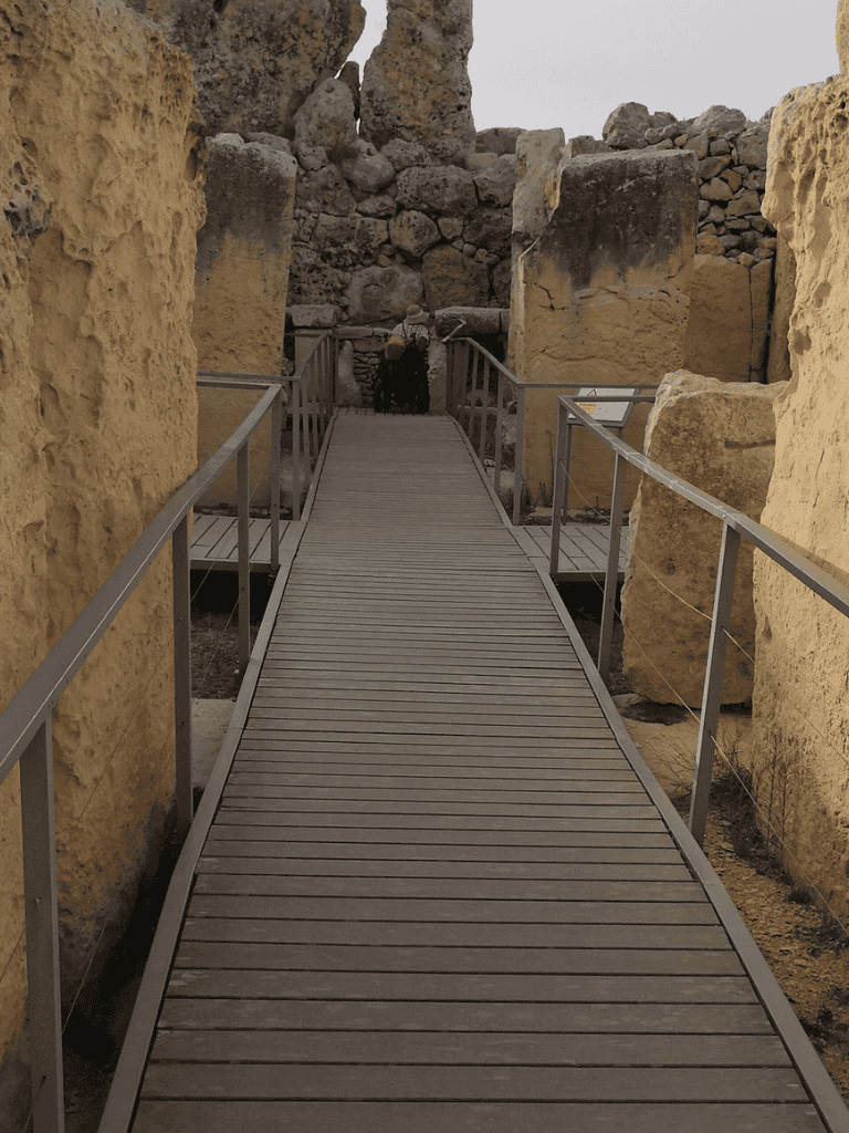 Ancient ruins with wooden pathway and stone walls, archaeological site explores desert history and architecture.