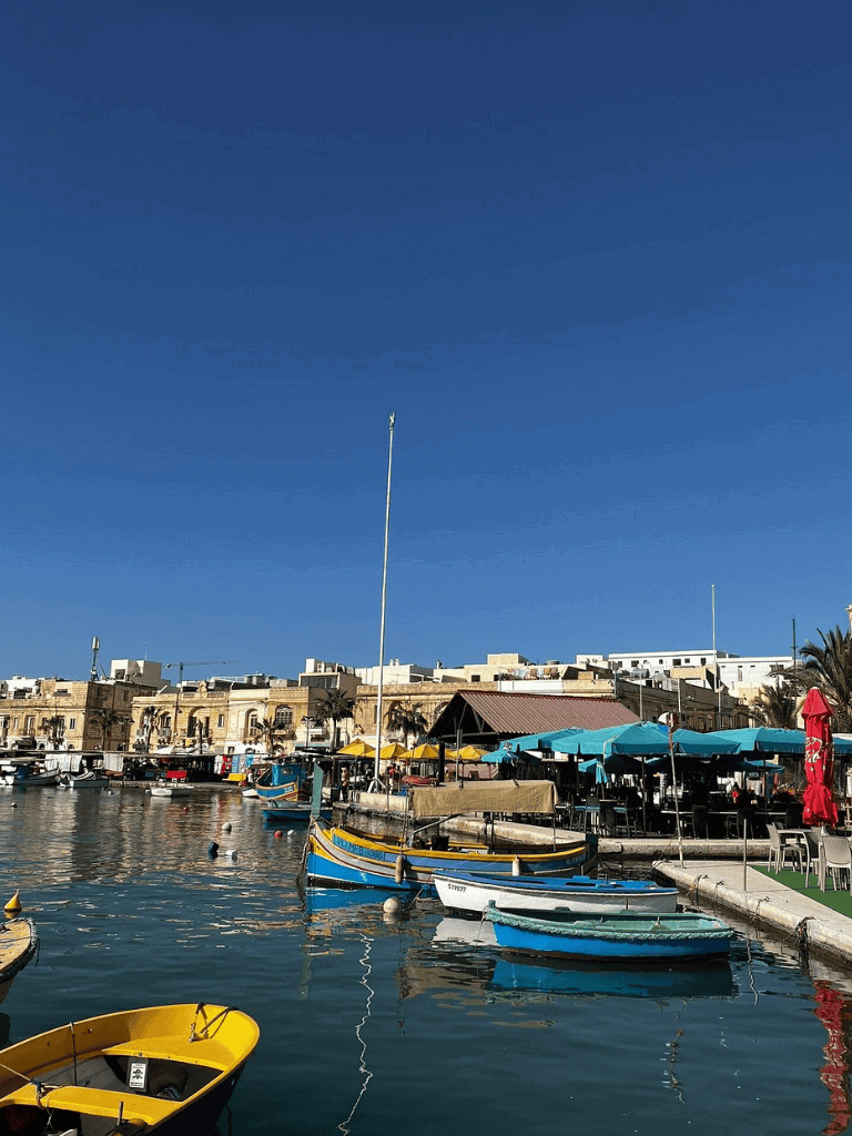 Colorful boats docked at a scenic harbor with historic buildings and clear blue sky.