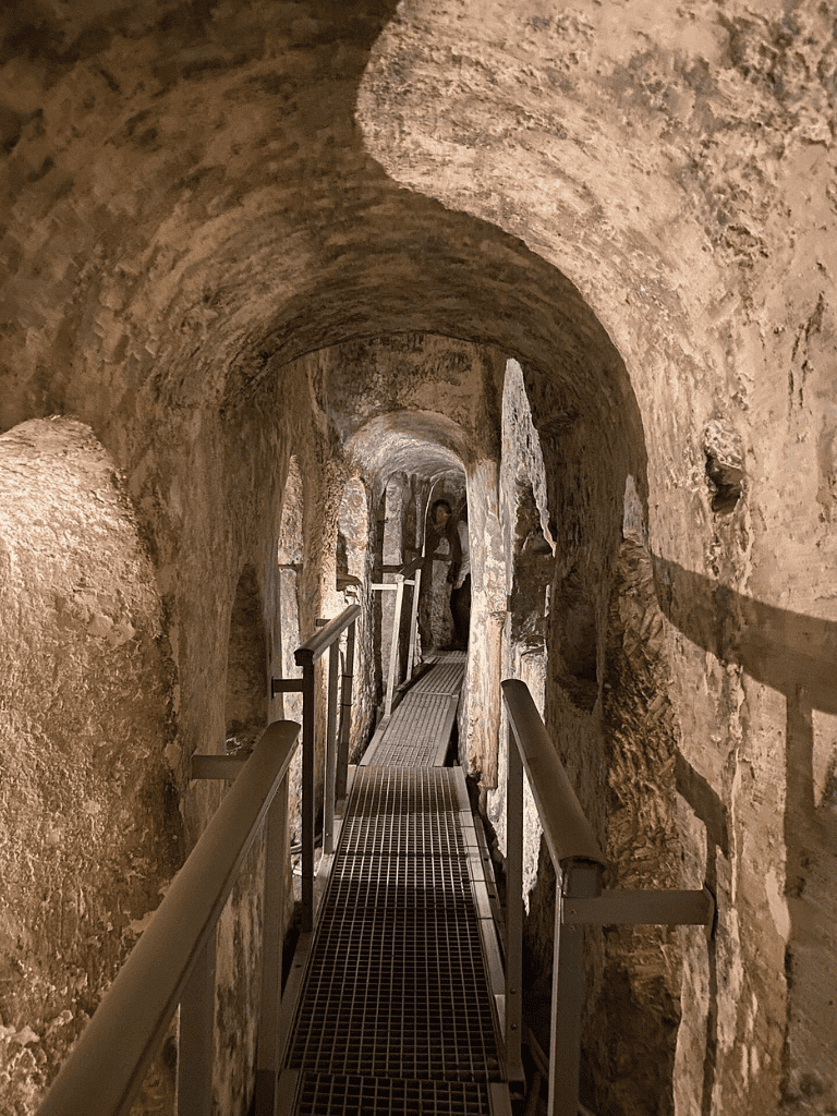Ancient stone cave tunnel with metal walkway and railings, exploring historic underground passageways.