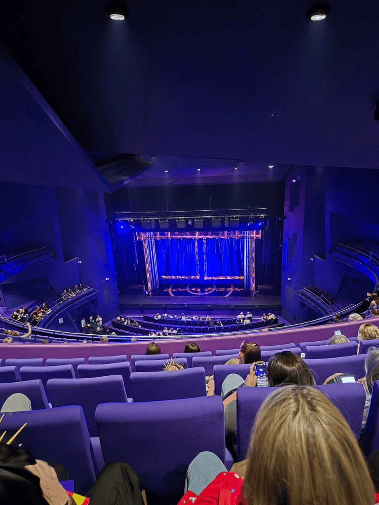 Modern theater interior with purple seats and a vibrant blue-lit stage, ideal for live performances and entertainment.