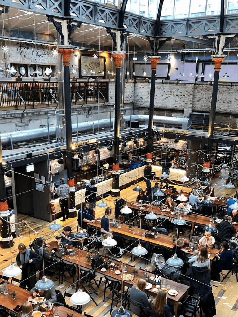 Cozy industrial-style restaurant with high ceilings, brick walls, and hanging pendant lights, lively dining atmosphere.