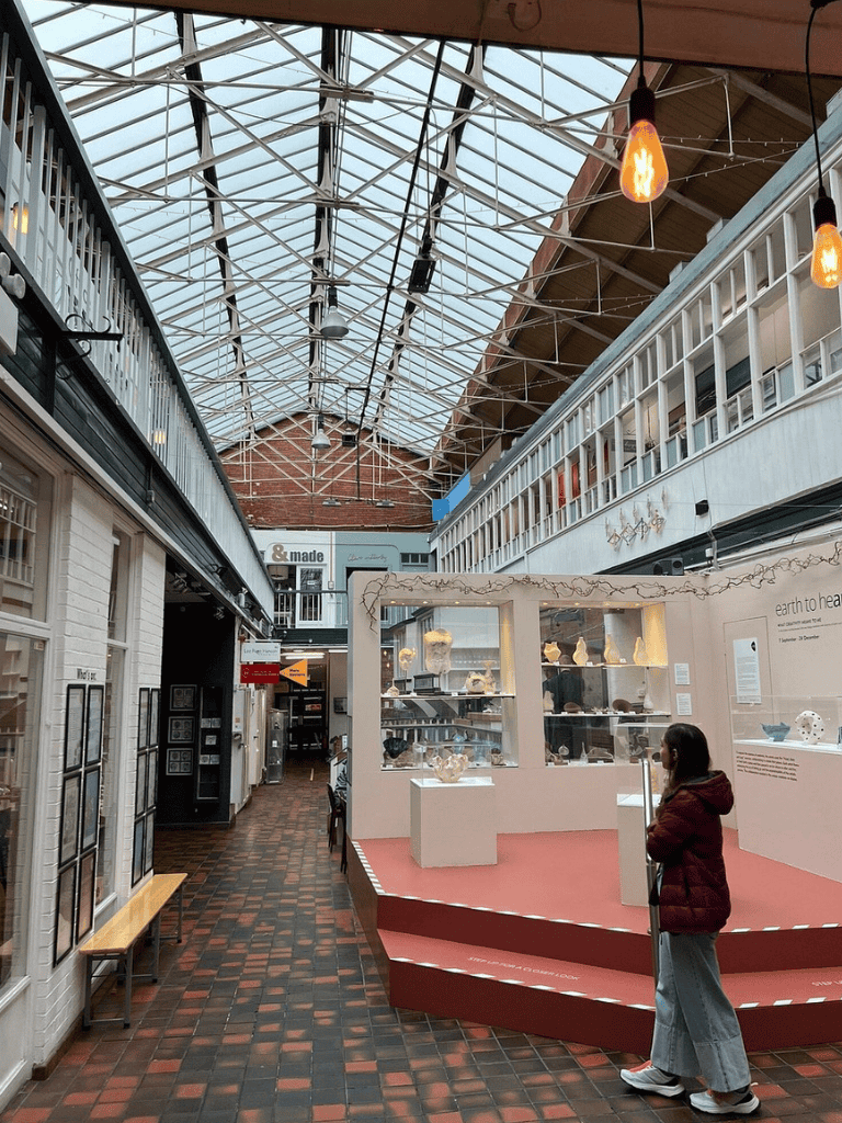 Colorful indoor shopping mall with glass ceiling, art displays, and a person viewing an exhibition.
