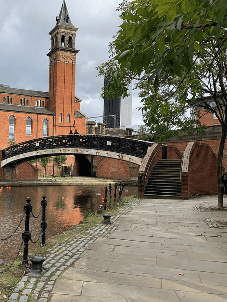 Historic brick church with clock tower by canal in city, featuring bridge and walkway scenic view.