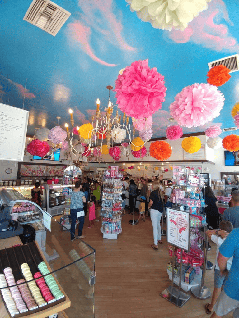 Pink and yellow tissue paper pom-poms hanging from a colorful sky-themed ceiling at a vibrant confectionery shop.
