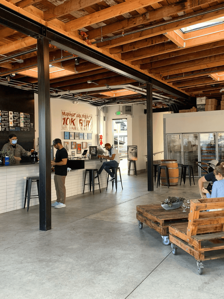 Open-concept brewery or café interior with exposed wooden beams, industrial design, and customers enjoying drinks.