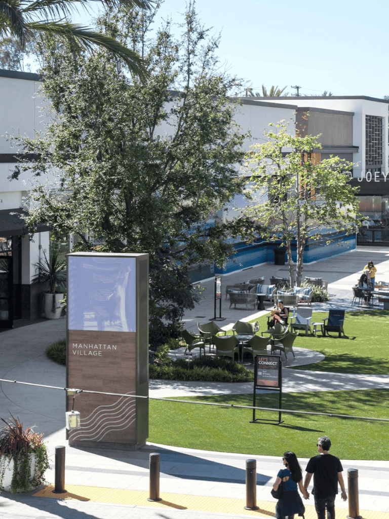 Modern outdoor shopping plaza with seating, greenery, and storefronts in Manhattan Village.