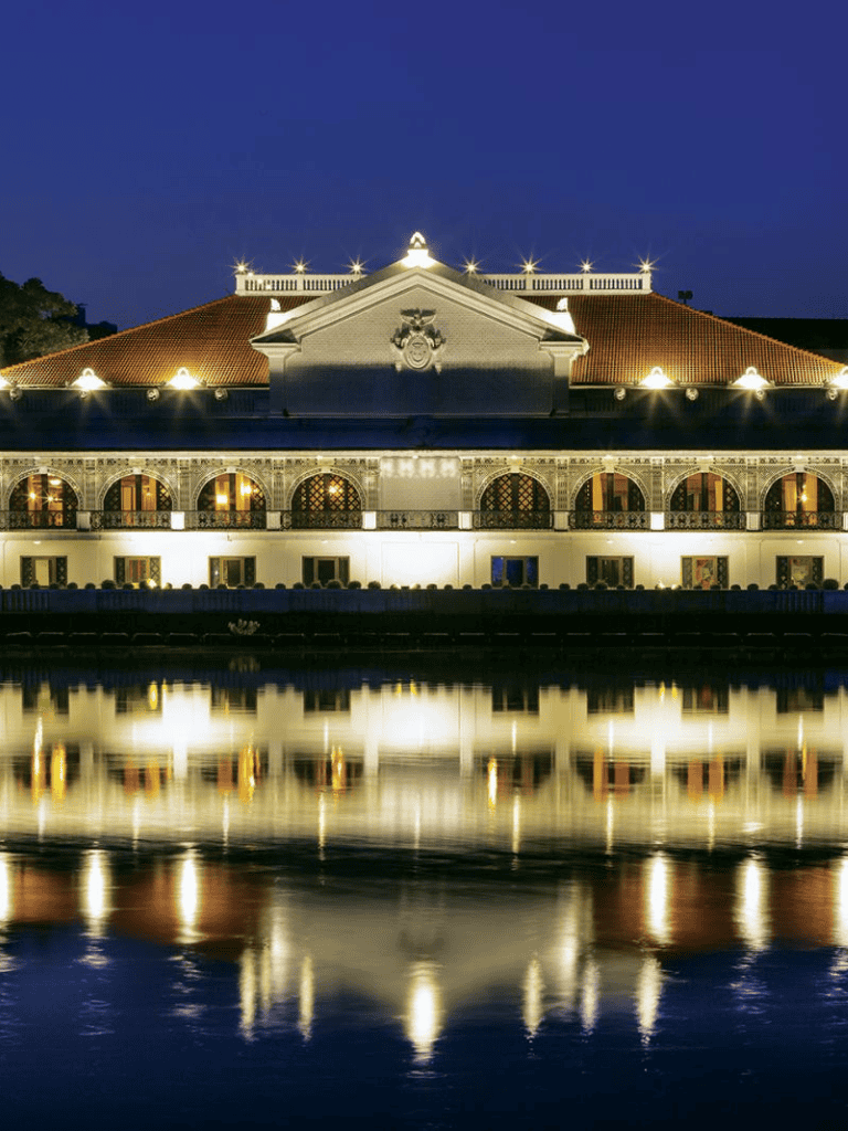 Luxury hotel illuminated at night with reflection on water, perfect for upscale travel or events.