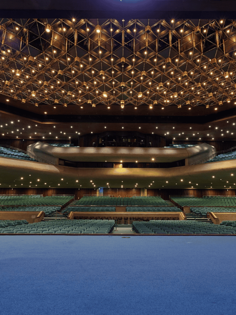 Brightly lit theatre auditorium interior with modern ceiling design and spacious seating arrangement.