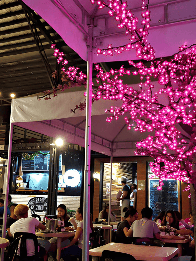 Bright pink cherry blossom LED lights in outdoor cafe at night, lively dining atmosphere, QuestForDirections.