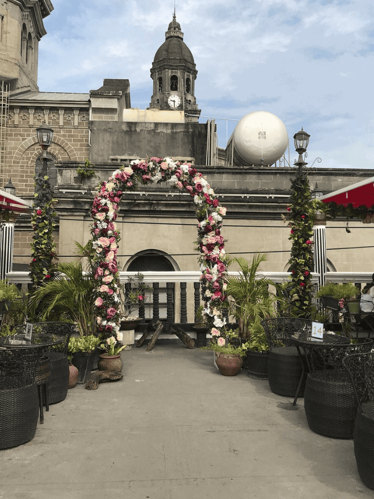Beautiful outdoor wedding setup with floral arch, cityscape background, and charming seating area.