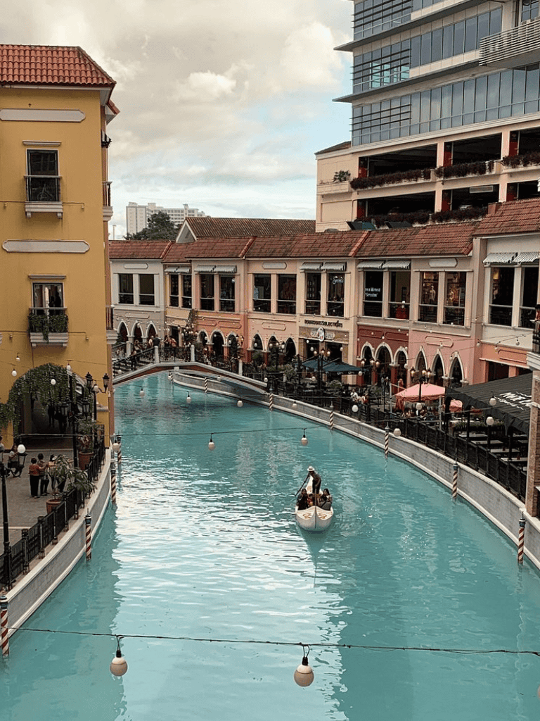 Elegant canal with gondola ride in a bustling shopping and dining district, featuring Mediterranean-style buildings.