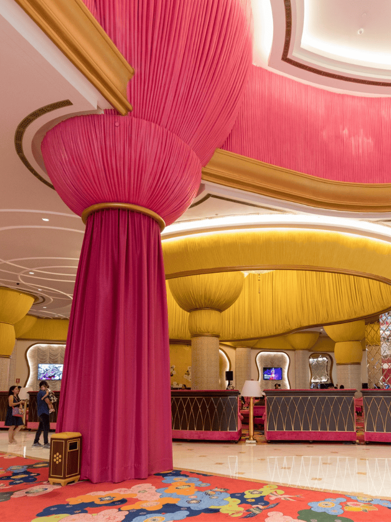 Luxurious hotel lobby with vibrant pink and yellow drapery, elegant columns, and modern decor.