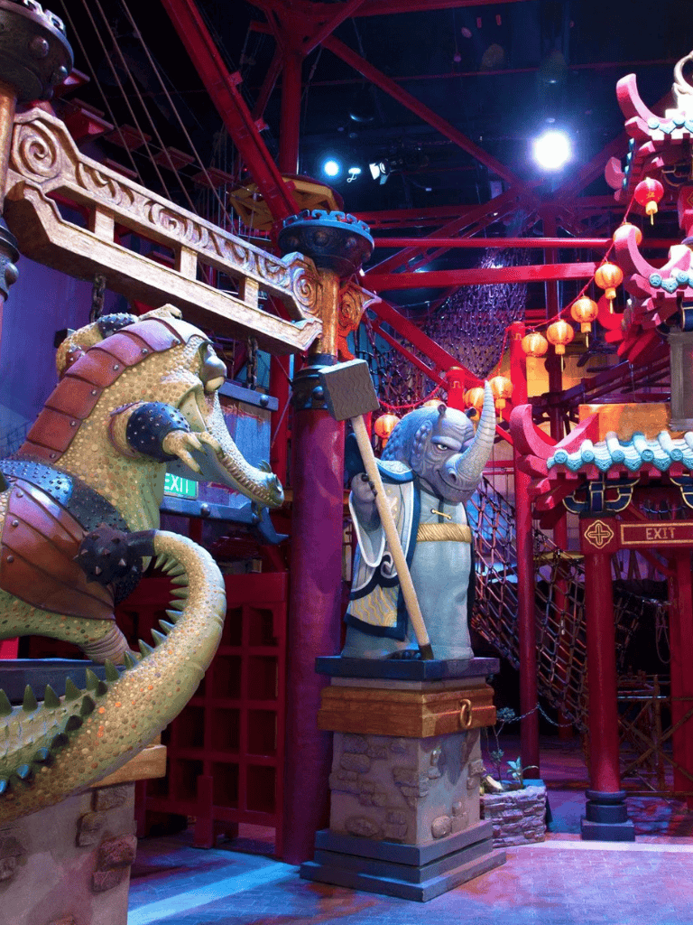 Colorful Asian-themed amusement park scene with dragon and elephant statues, vibrant red structures, and traditional decorations.