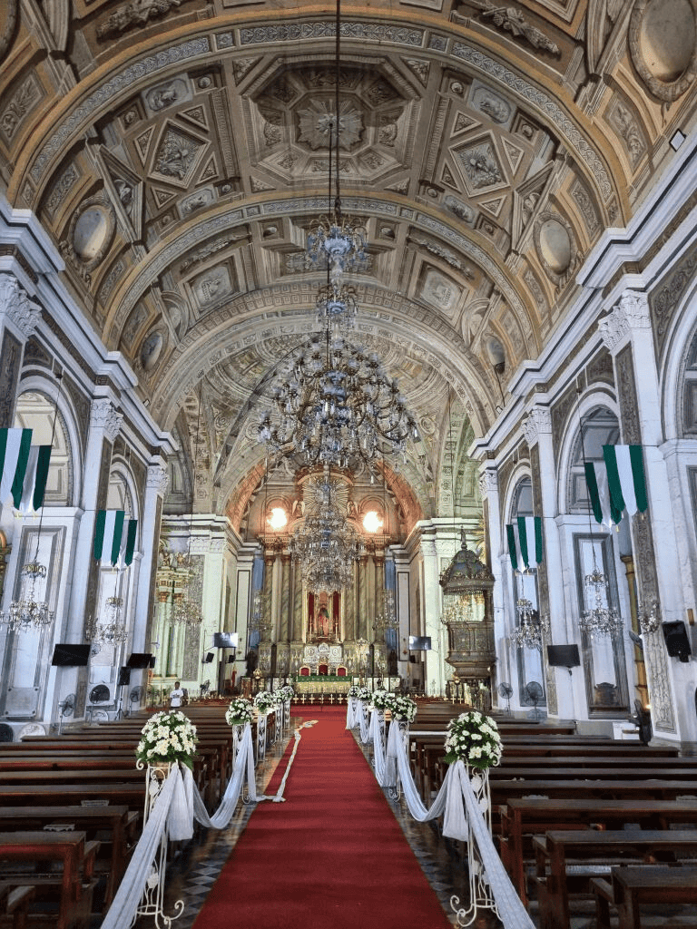 Ornate church interior with chandeliers, high vaulted ceiling, and wedding ceremony setup.