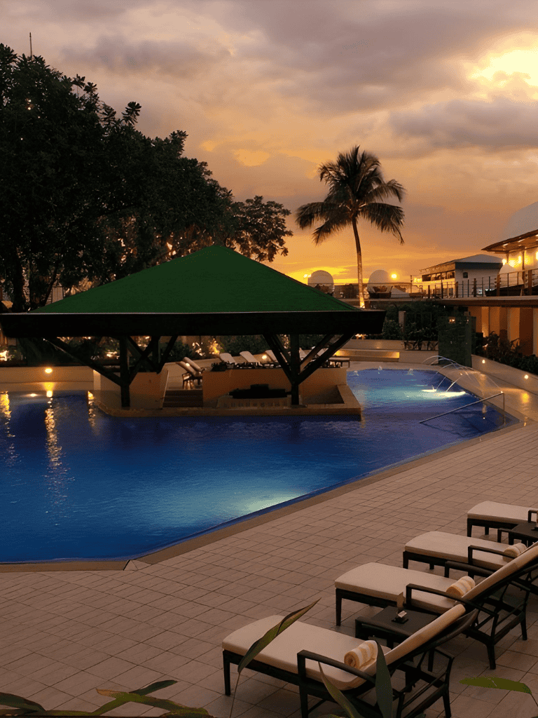 Serene swimming pool scene at dusk with palm trees and modern resort buildings, ideal for vacation relaxation.