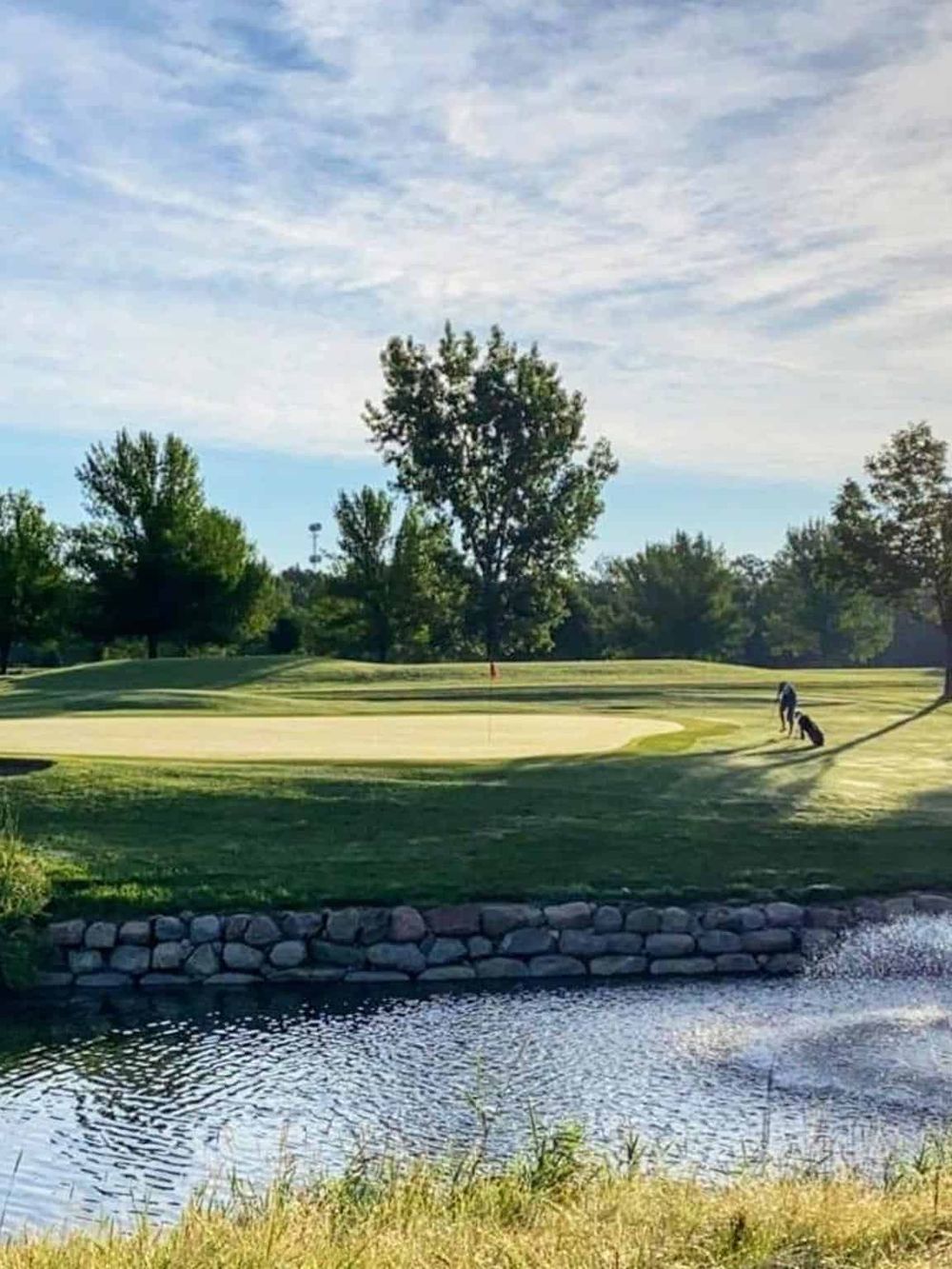 Serene golf course with water feature, lush greenery, and a golfer preparing for a shot. Perfect setting for outdoor recreational activities.