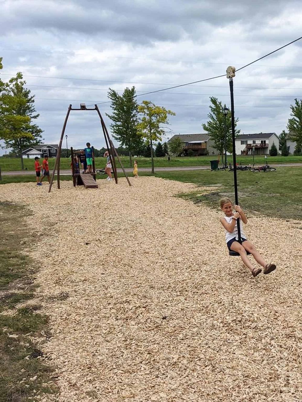 Children playing on playground swing set with a young girl smiling, outdoor park scenery, family-friendly activities, kids enjoying nature.