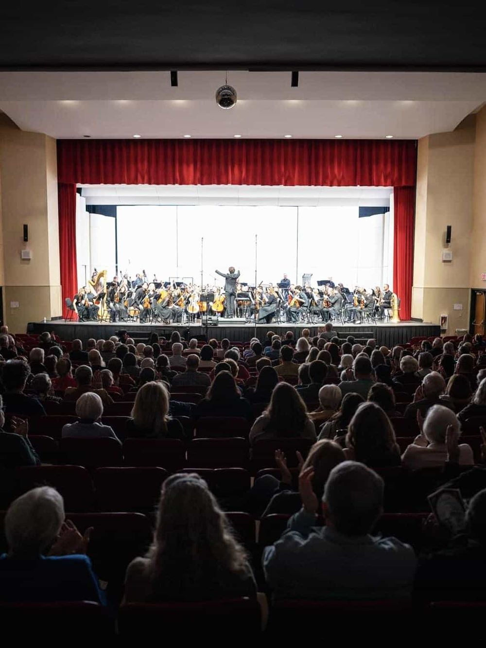 Orchestra performing on stage at a concert hall with audience watching.