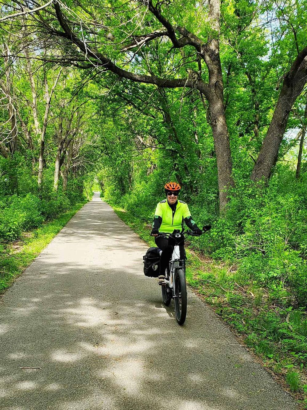 Bright cyclist riding on a green trail surrounded by leafy trees and lush vegetation.