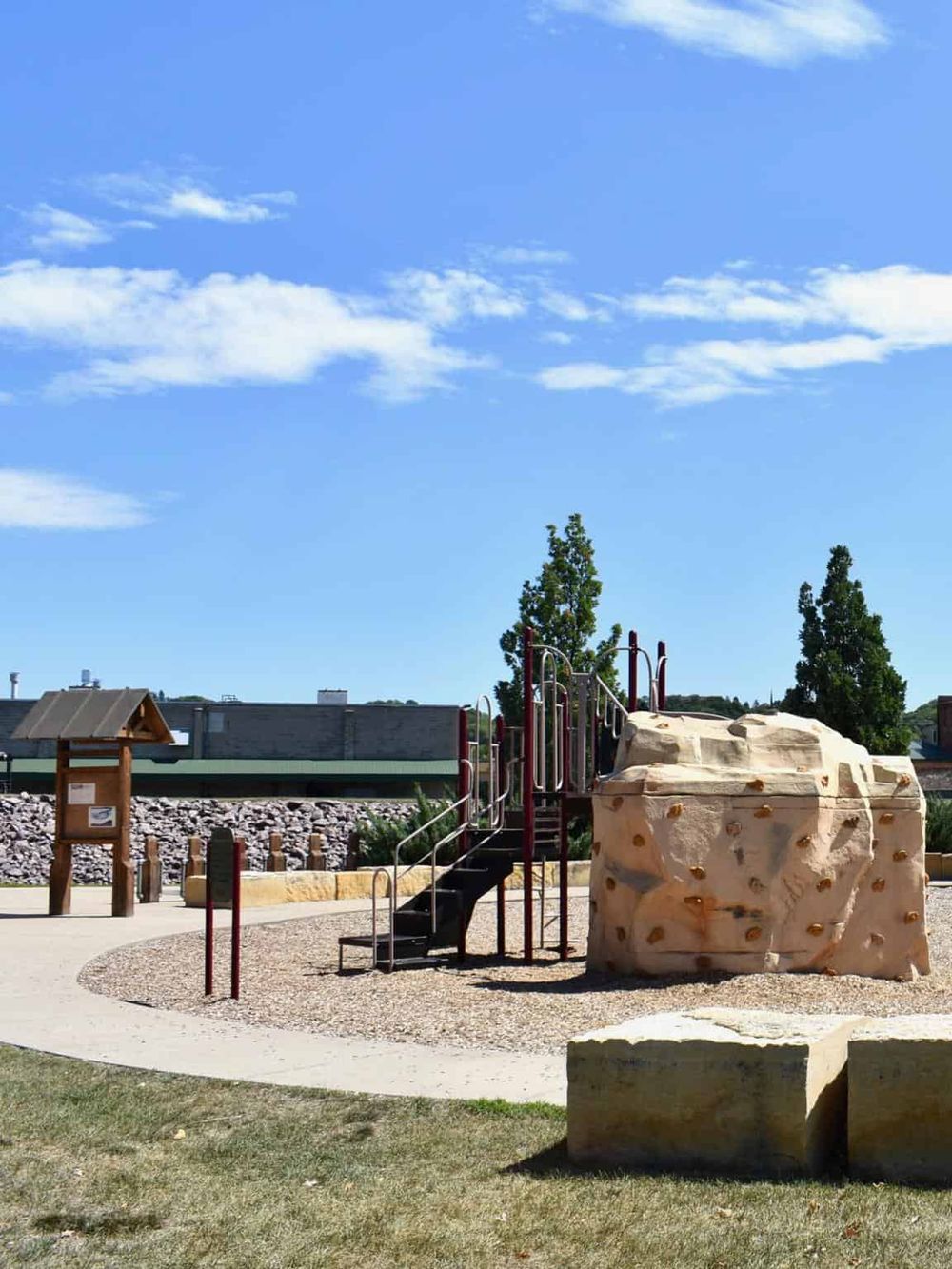 Colorful outdoor playground with rock climbing structure and slide, set against a clear blue sky and trees.