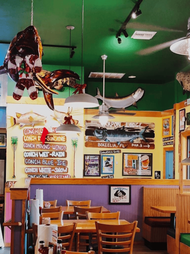 Colorful seafood restaurant interior with hanging fish decorations and tropical-themed menu signs promoting conch dishes.