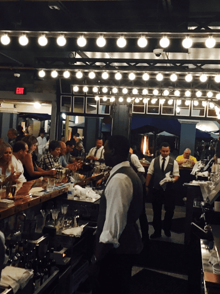 Sleek bar with bartenders serving customers in a lively, modern restaurant ambiance.