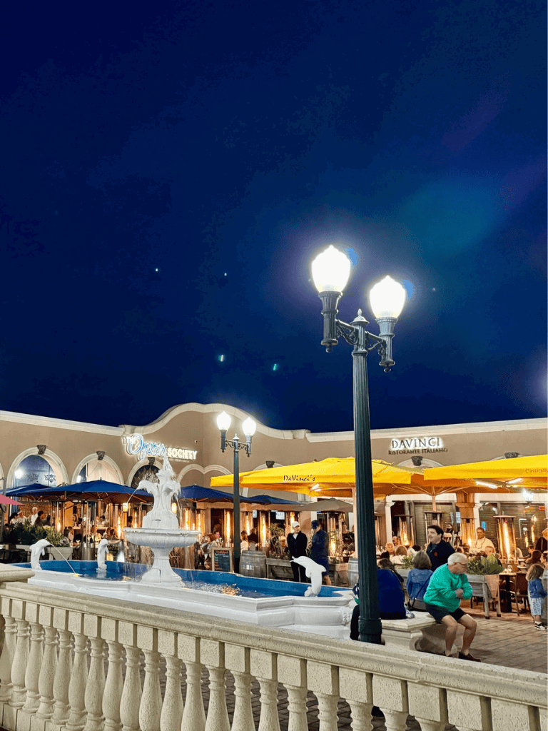 Colorful outdoor dining area with a fountain and street lamps at night, perfect for food lovers.